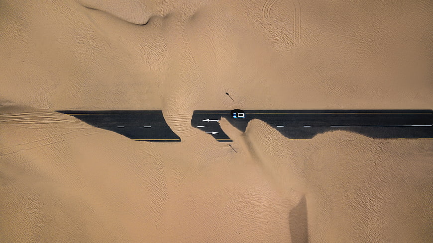 Aerial view of car on desert road partially covered by sand