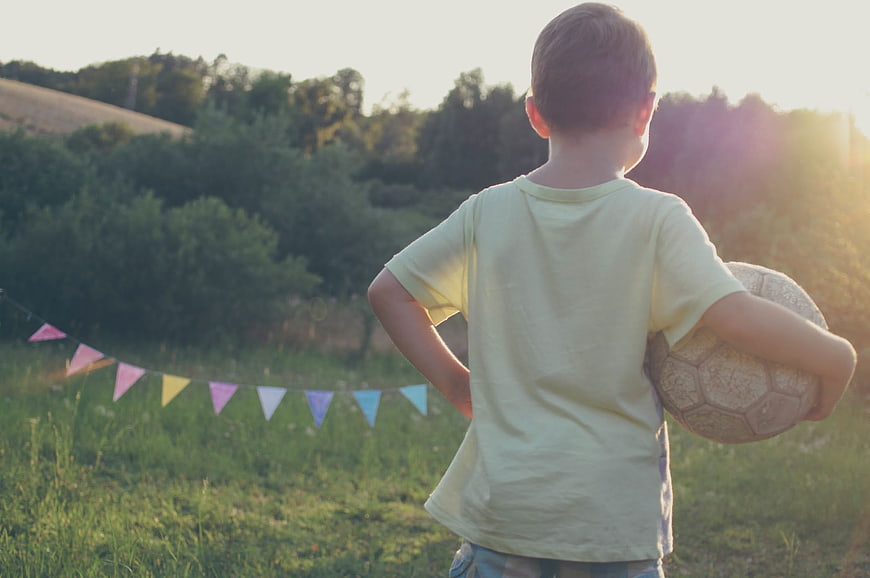 Young Boy Holding Soccer Ball in Field at Sunset