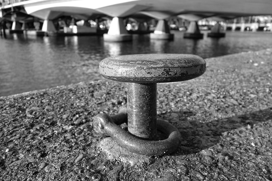 Close-up of weathered metal mooring bollard on concrete quay