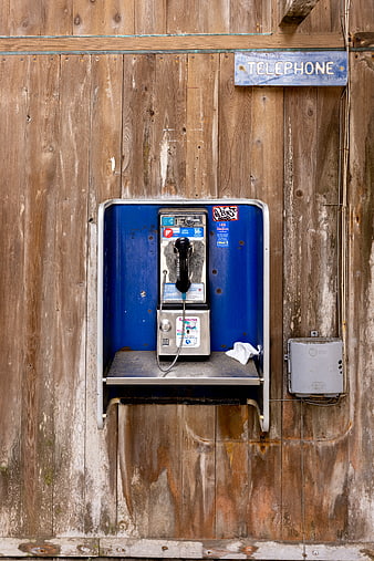 Vintage blue payphone mounted on weathered wooden wall