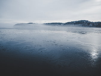 Foggy Frozen Lake Landscape with Snowy Forest Background