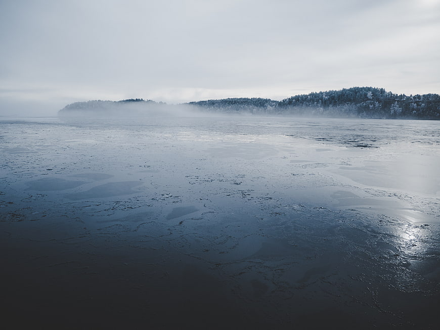 Foggy Frozen Lake Landscape with Snowy Forest Background