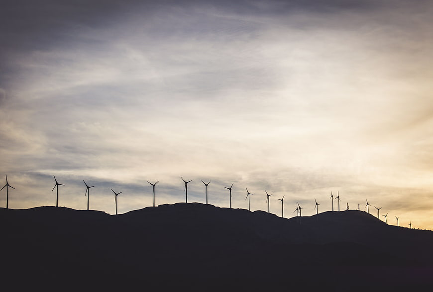 Silhouette of wind turbines on a hill against a cloudy sunset sky