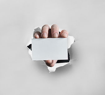 Hand holding blank business card through torn paper hole