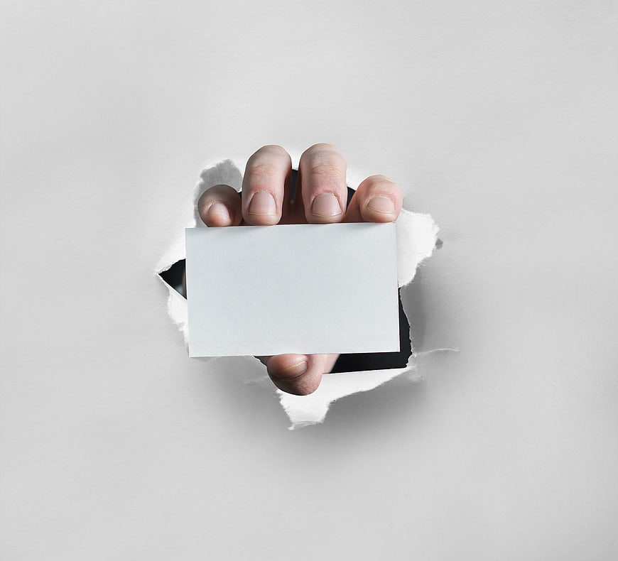 Hand holding blank business card through torn paper hole