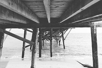 Black and white view under wooden pier pilings at the beach
