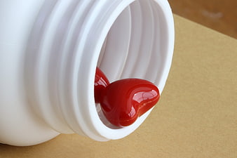 Red Heart-Shaped Capsule Spilling From White Medicine Bottle