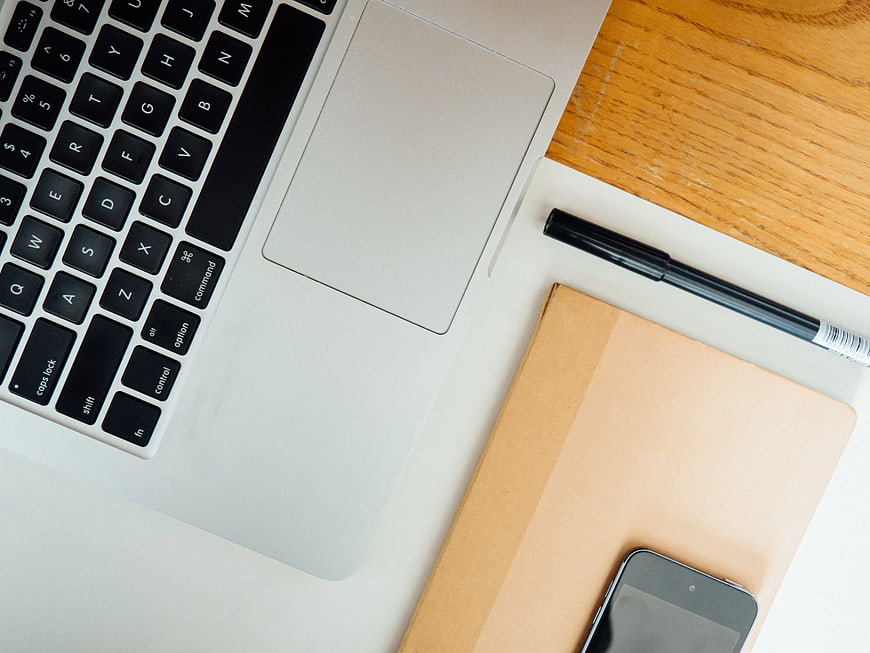 Flat lay of laptop, notebook, pen, and smartphone on wooden desk