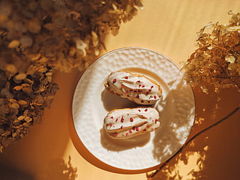 Top view of glazed eclairs with dried flowers on orange background