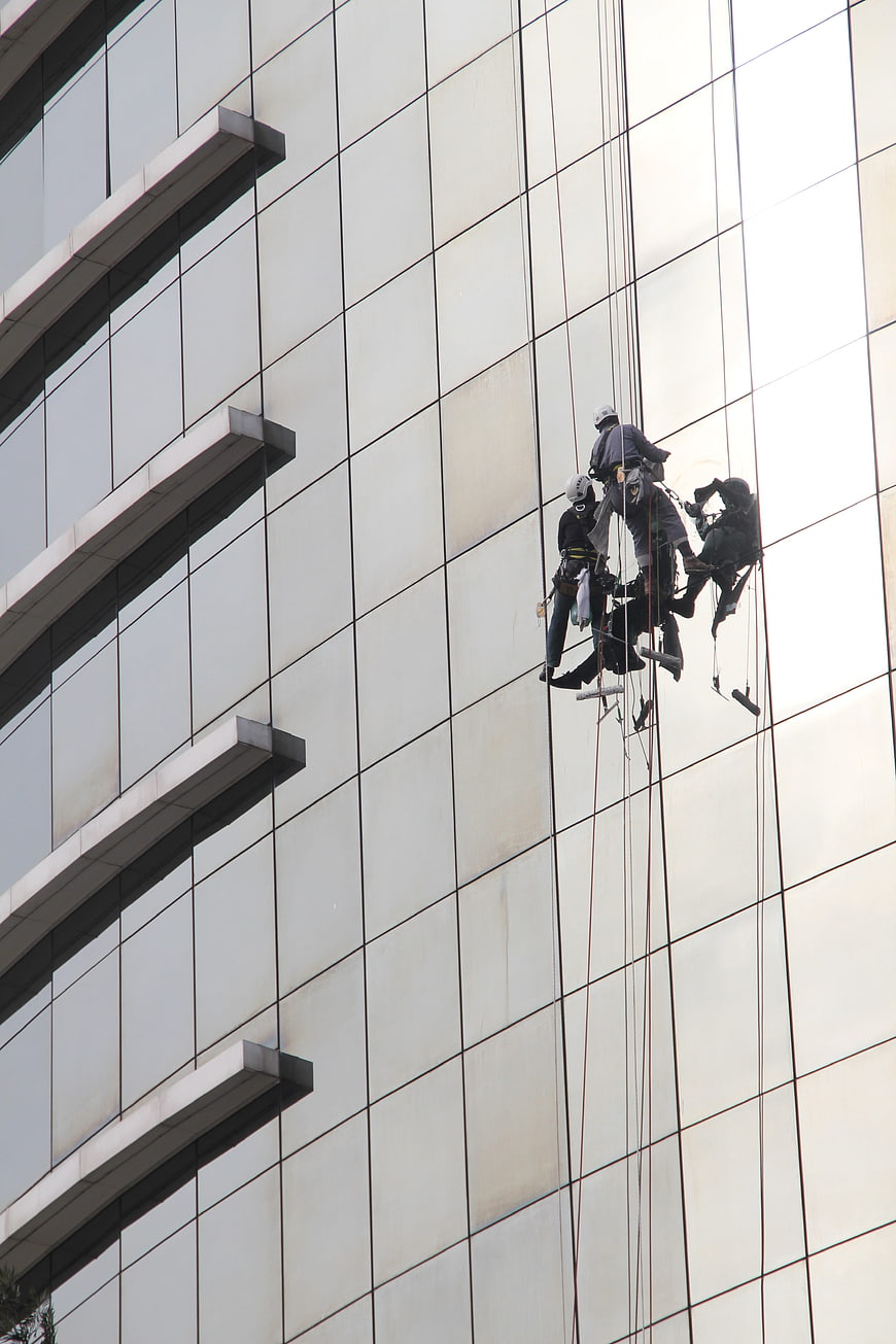 Window Cleaners Rappelling on Modern Glass Skyscraper Facade