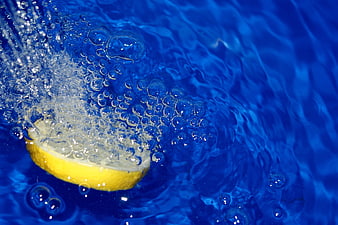 Lemon slice splashing into blue water with bubbles