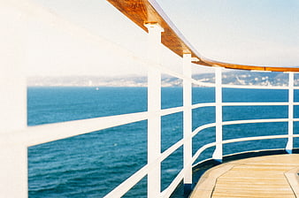 White ship railing on wooden deck overlooking blue sea
