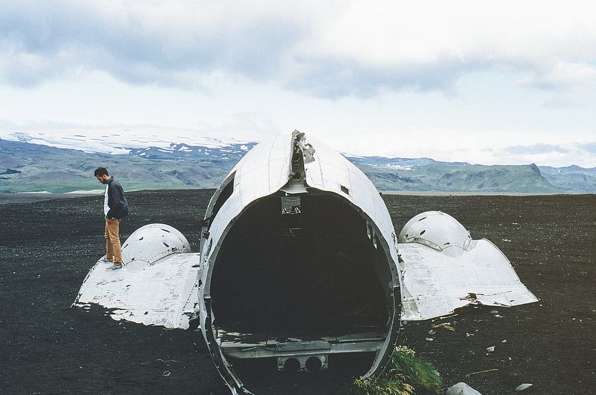 Man standing on airplane wreck on black sand beach