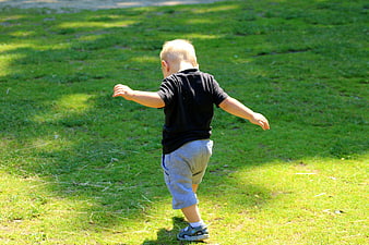 Toddler boy taking first steps on green grass in a sunny park