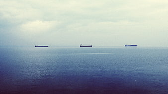 Three cargo ships on calm blue sea under cloudy sky