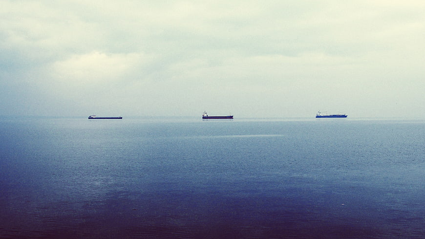 Three cargo ships on calm blue sea under cloudy sky