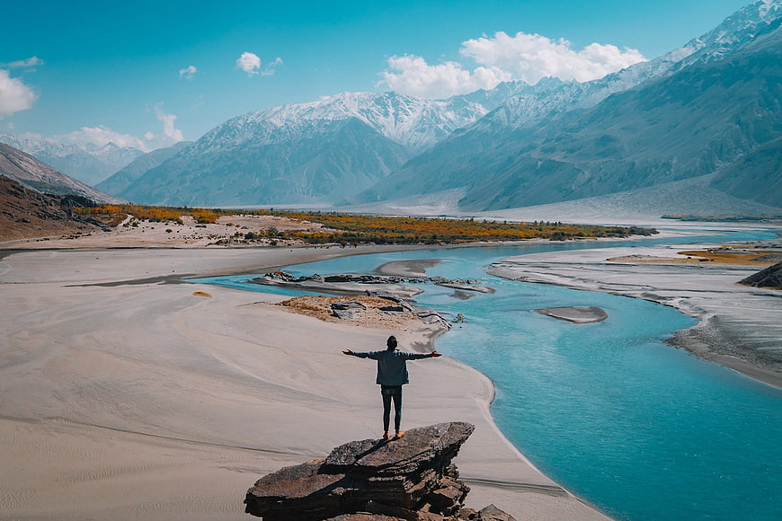 Man standing on rock overlooking turquoise river and mountains