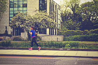 Woman jogging on city sidewalk near modern building