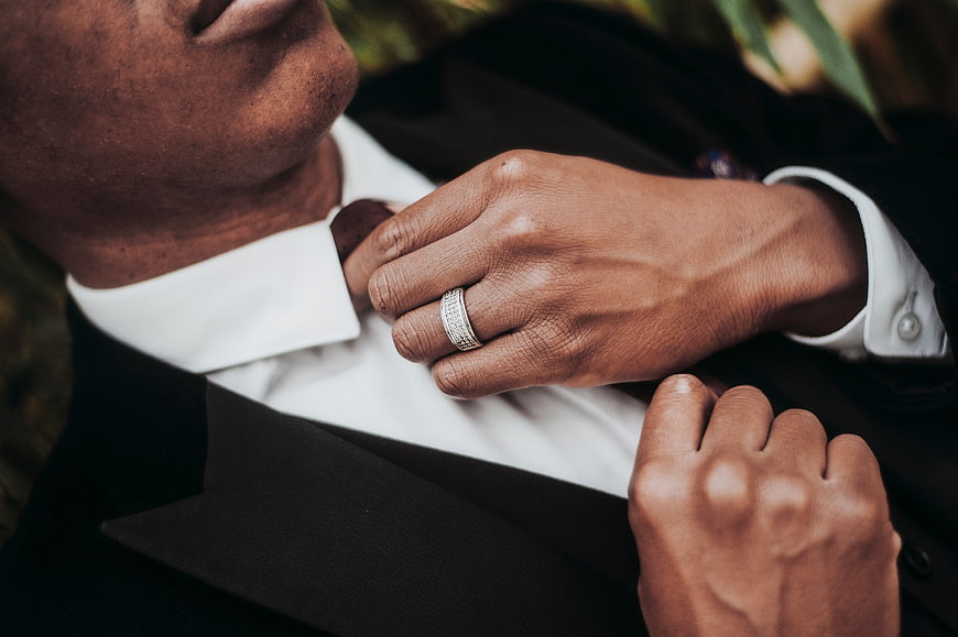 Close-up of groom adjusting tie with diamond ring