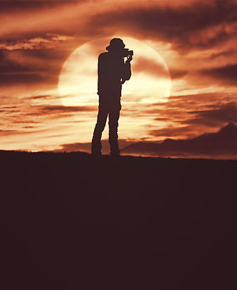 Silhouette of Photographer Filming Sunset Over Mountains