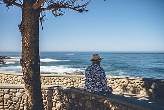 Man in Hawaiian Shirt Sitting on Stone Wall by Ocean