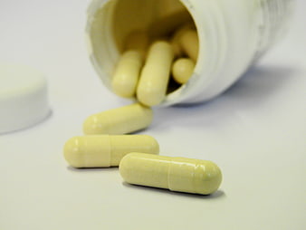 Yellow capsules spilling from white bottle on white background