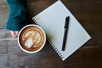 Flat lay of latte art, notebook, and pen on wooden table