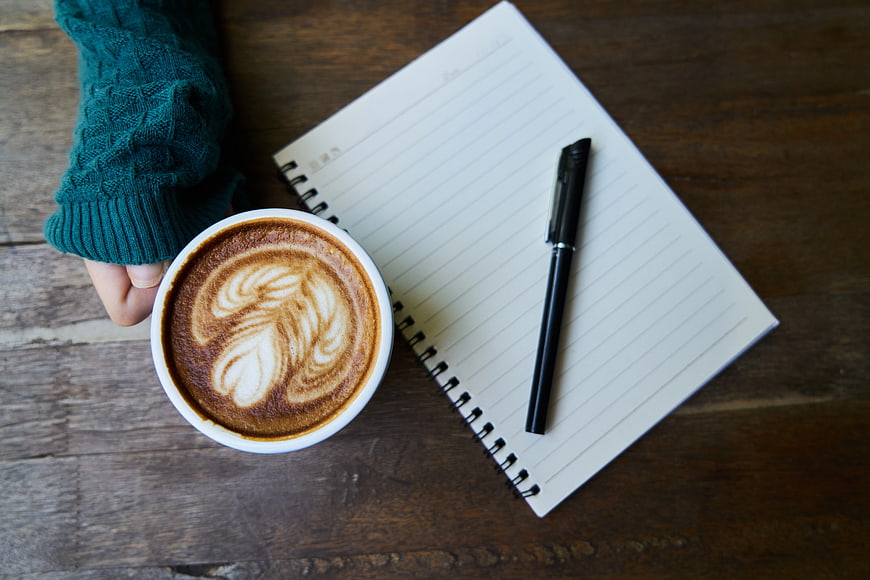 Flat lay of latte art, notebook, and pen on wooden table