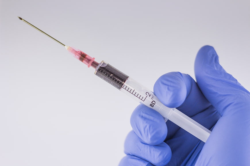 Blue Gloved Hand Holding Medical Syringe with Needle