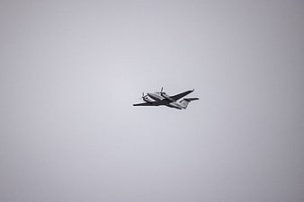 Twin-engine propeller airplane flying in gray sky