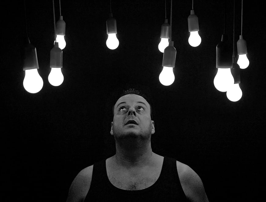 Man looking up at hanging light bulbs in black and white