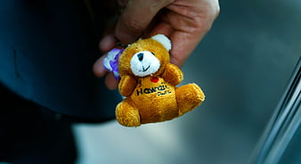 Hand holding small brown teddy bear souvenir keychain