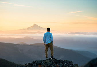 Man standing on mountain peak looking at sunrise over clouds