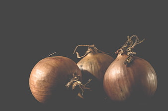 Three Raw Brown Onions With Dried Tops On Dark Gray Background