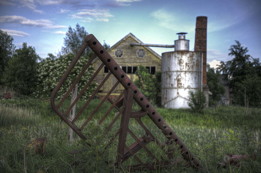 Rusty Farm Equipment in Overgrown Field with Barn
