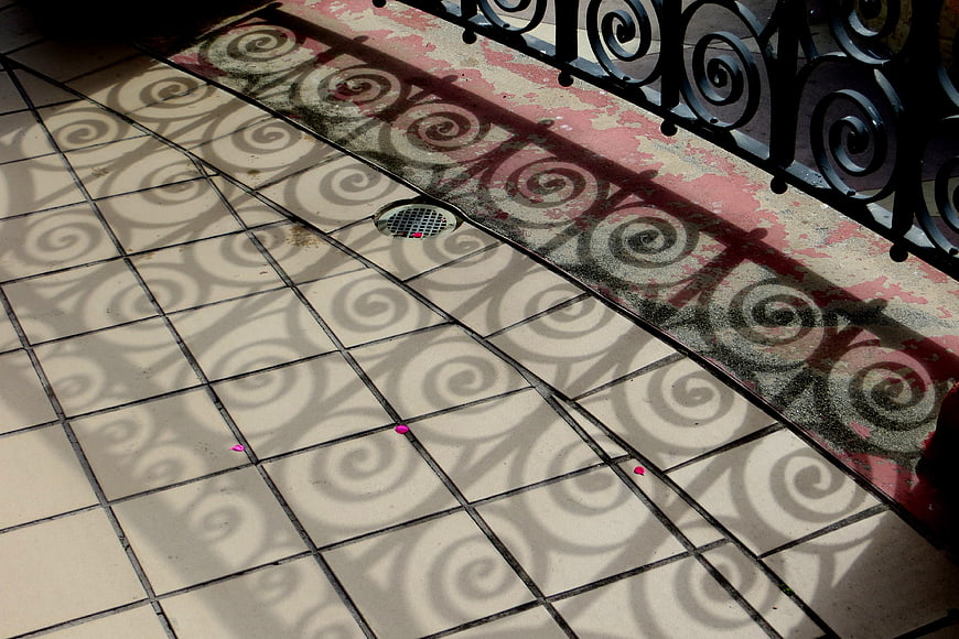 Spiral shadows cast by wrought iron railing on tiled floor
