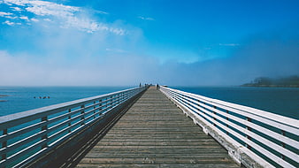 Wooden pier extending into blue ocean with foggy horizon