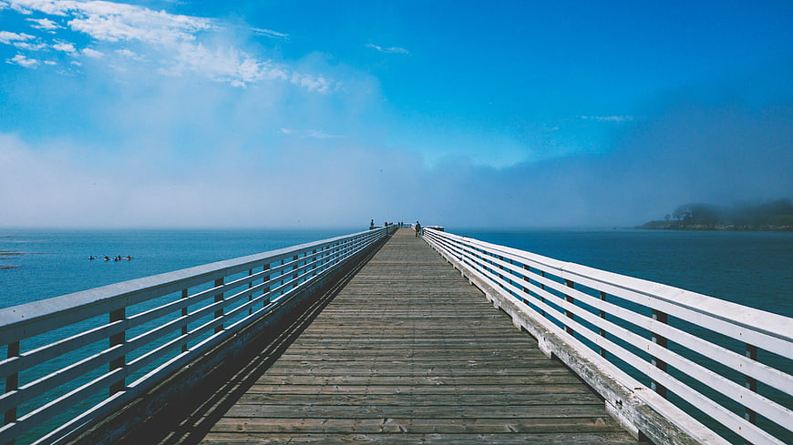 Wooden pier extending into blue ocean with foggy horizon
