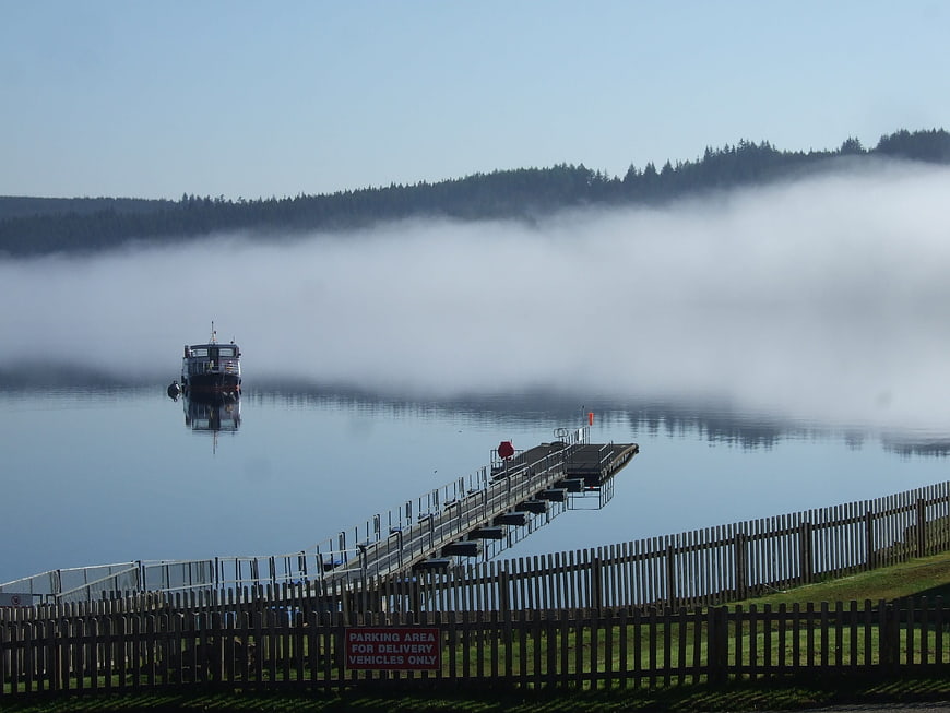 Ferry boat on misty lake with wooden jetty and forest background