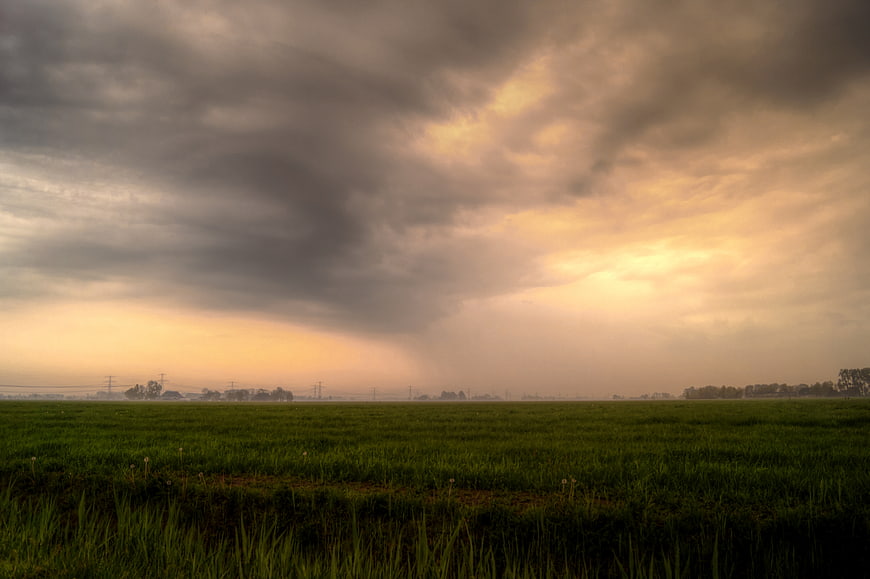 Dramatic sunset over green meadow with storm clouds