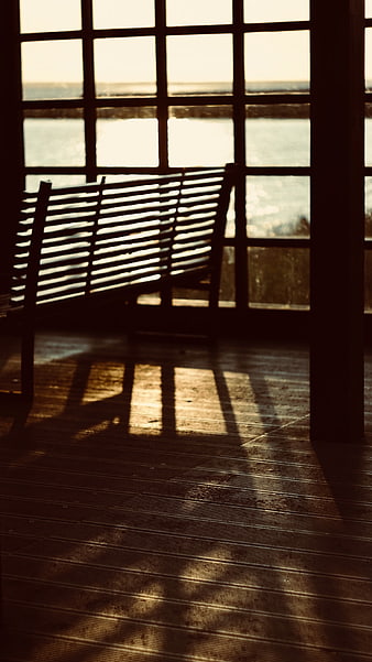 Sunlit wooden bench silhouette with window shadows on deck