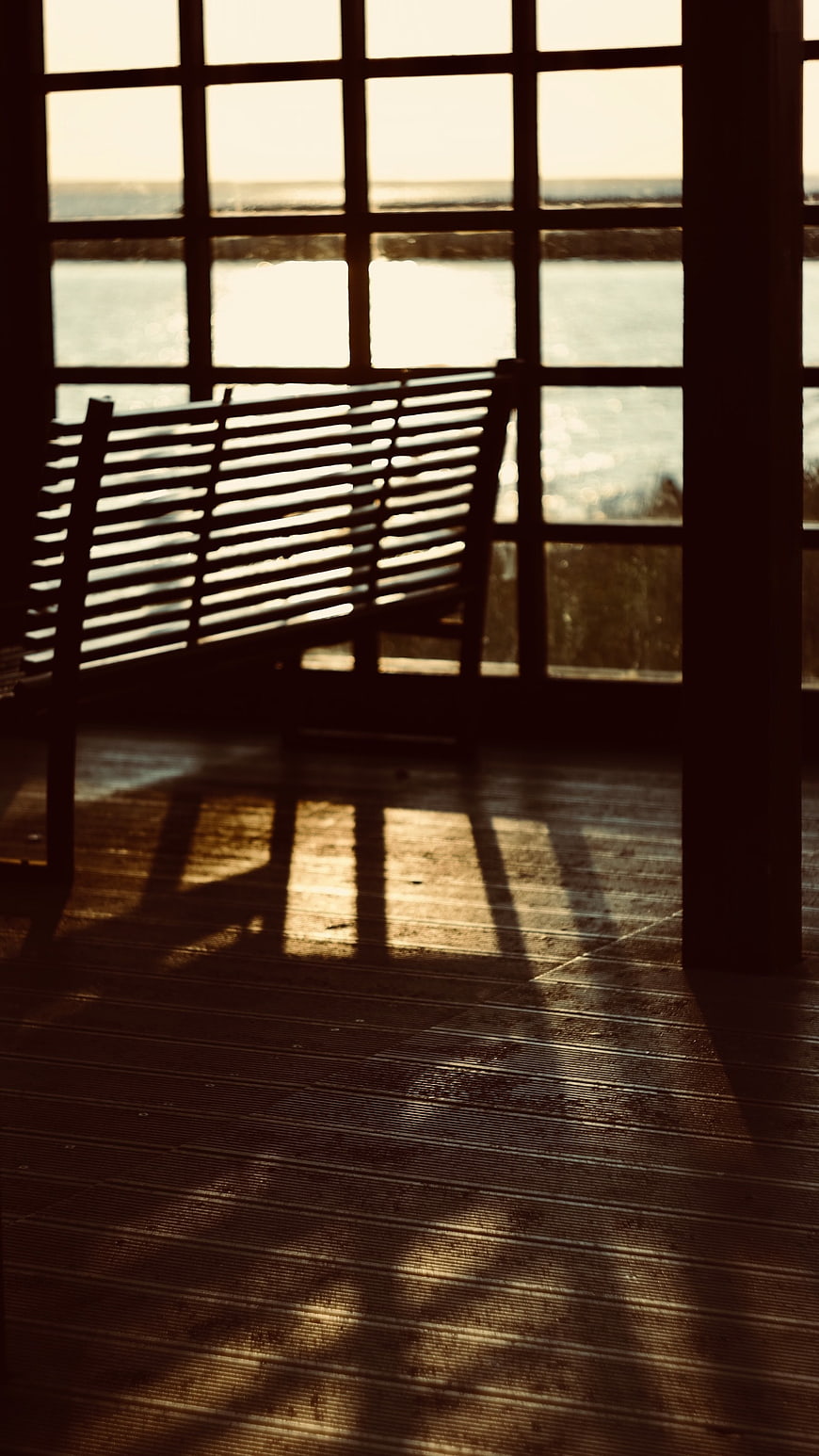 Sunlit wooden bench silhouette with window shadows on deck