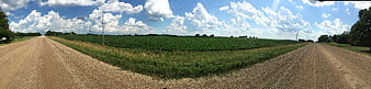 Panoramic rural dirt road intersection with green fields and blue sky