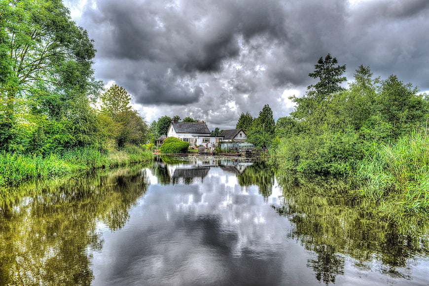 Cottage on River Bank Under Stormy Clouds