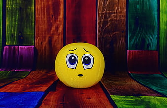 Yellow Sad Emoji Ball on Colorful Wooden Background