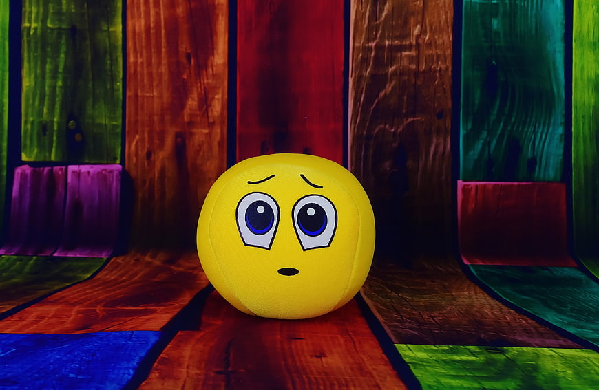 Yellow Sad Emoji Ball on Colorful Wooden Background