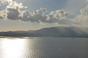 Sunbeams over ocean with distant mountains and ships