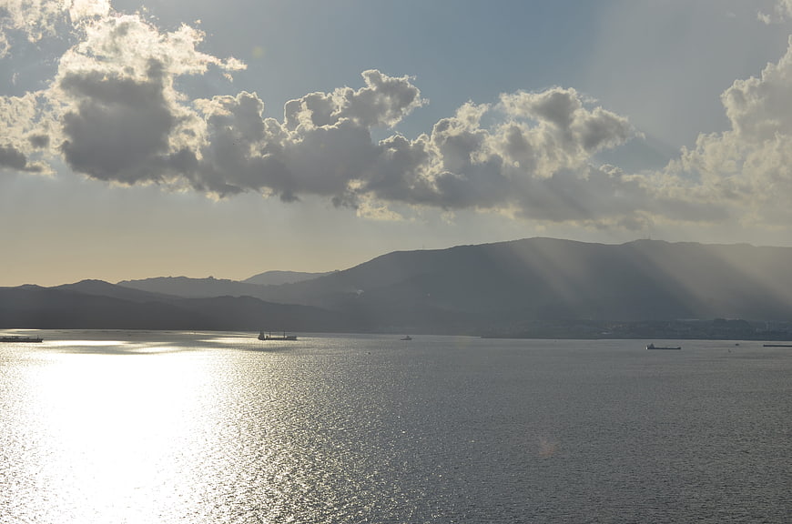 Sunbeams over ocean with distant mountains and ships