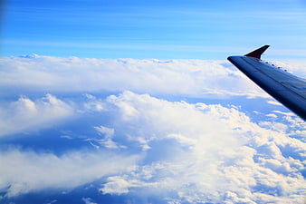 Airplane wing flying above clouds in blue sky
