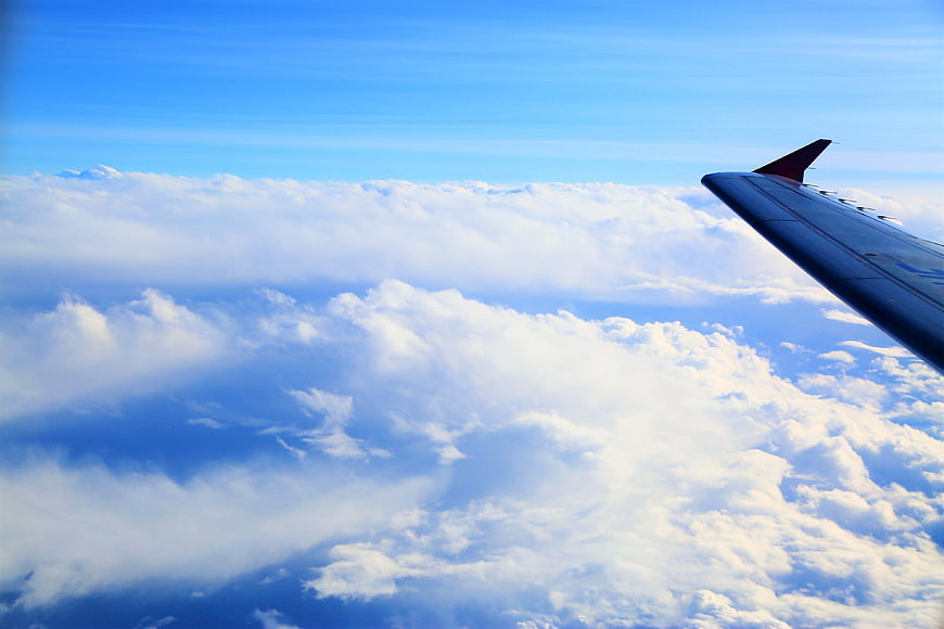 Airplane wing flying above clouds in blue sky